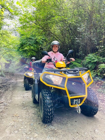 A person riding a yellow ATV on a dirt path surrounded by dense green foliage. 3
