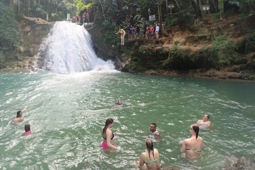 A waterfall, people swimming, and a group of people on a cliff. 1