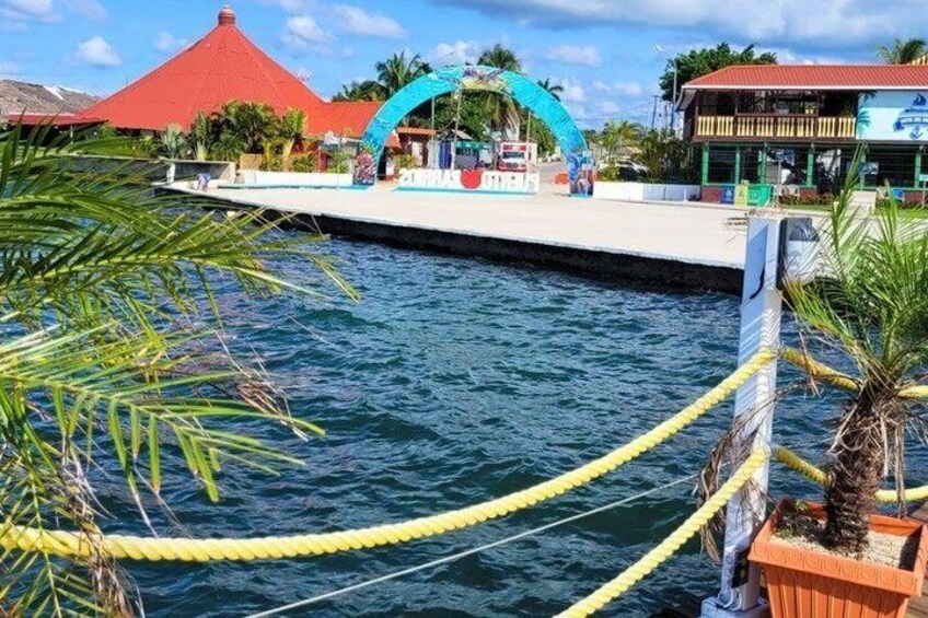 A waterfront with a red-roofed building, a blue archway, and a wooden dock. 3