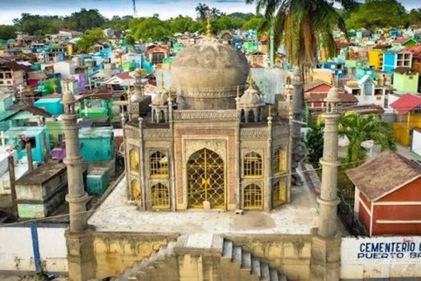 A mausoleum with a dome and arched windows, surrounded by colorful buildings and palm trees. 3