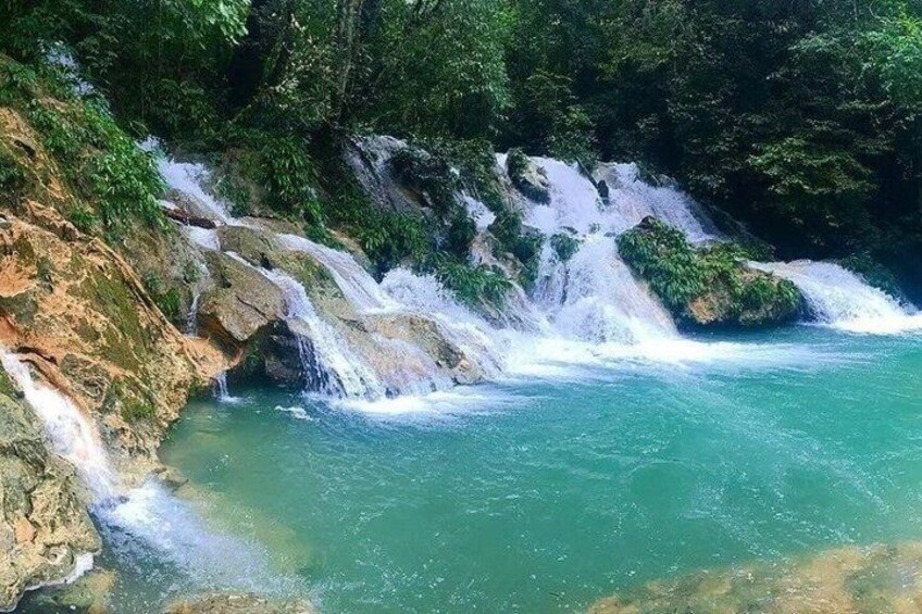 A waterfall cascading over rocks into a turquoise pool surrounded by dense green foliage. 2