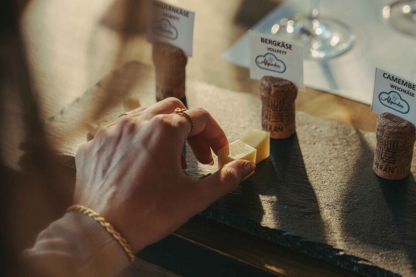 A hand selecting a cheese from a wooden board with labels indicating different types of cheese. 3