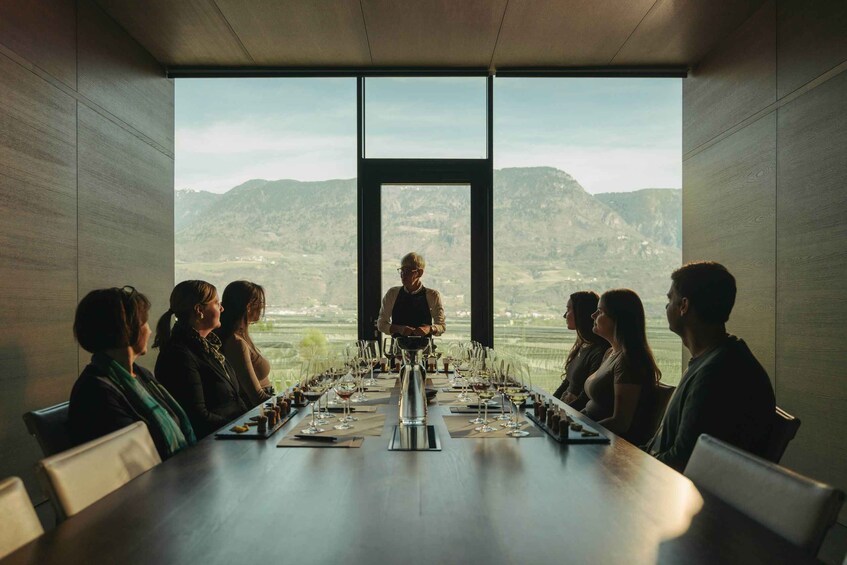A group of people seated around a long table with a view of a mountainous landscape through a large window. 1