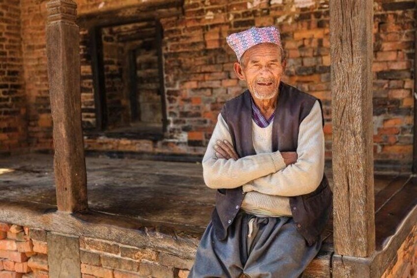 An elderly man sitting on a wooden bench in a rustic brick building. 2
