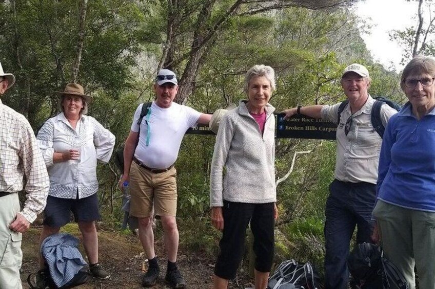 A group of hikers on a trail with a sign indicating directions to Broken Hills Carpark. 4