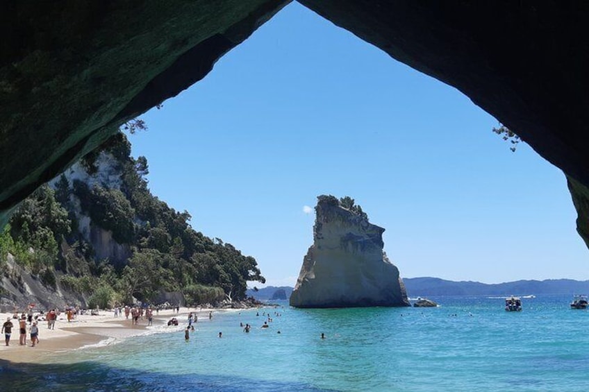 A beach with clear turquoise water, a prominent rock formation, and a forested cliff. 1