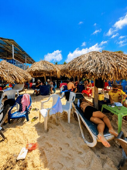 A beach with thatched umbrellas, lounge chairs, and people sunbathing. 2