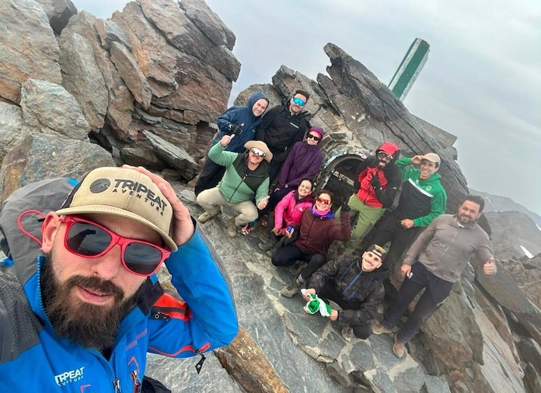 A group of people on a rocky mountain with a green structure in the background. 4