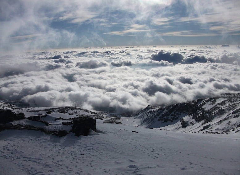 A snow-covered mountain landscape with a dense layer of clouds below. 3