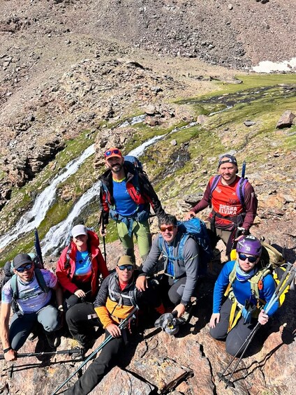 A group of hikers on a rocky mountain trail with a waterfall in the background. 2