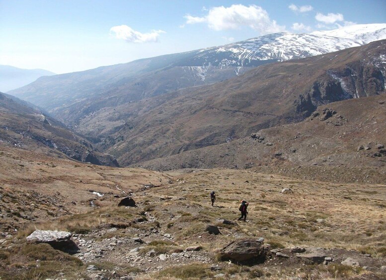 A mountainous landscape with hikers, rocky terrain, and a snow-capped peak in the distance. 5