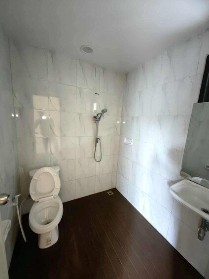 A bathroom with white marble tiles, a toilet, a shower, and a sink. 3