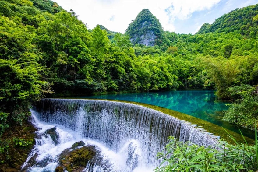 A waterfall cascading into a clear turquoise lake surrounded by lush green forest. 1