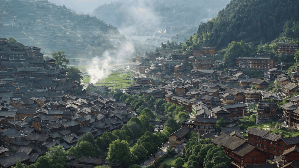 A traditional village with tiered houses, a river, and misty mountains in the background. 2