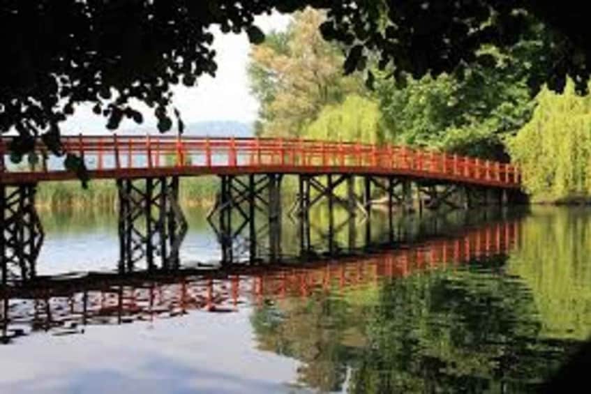 A red bridge over a calm body of water with trees on either side. 2