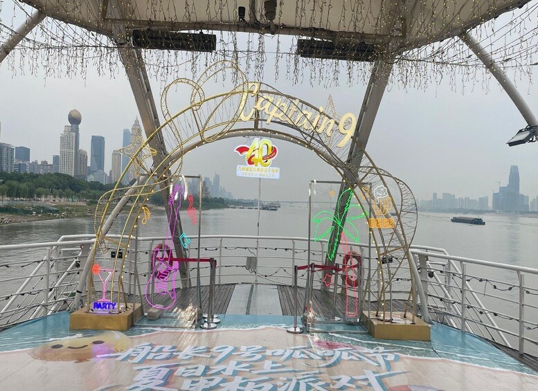 A boat deck with a city skyline in the background, a neon sign, and decorative lights. 2