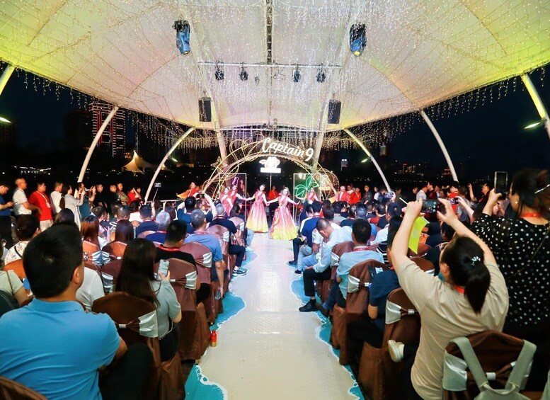 A stage with performers in costumes, an audience seated in rows, and a decorative archway with lights. 3