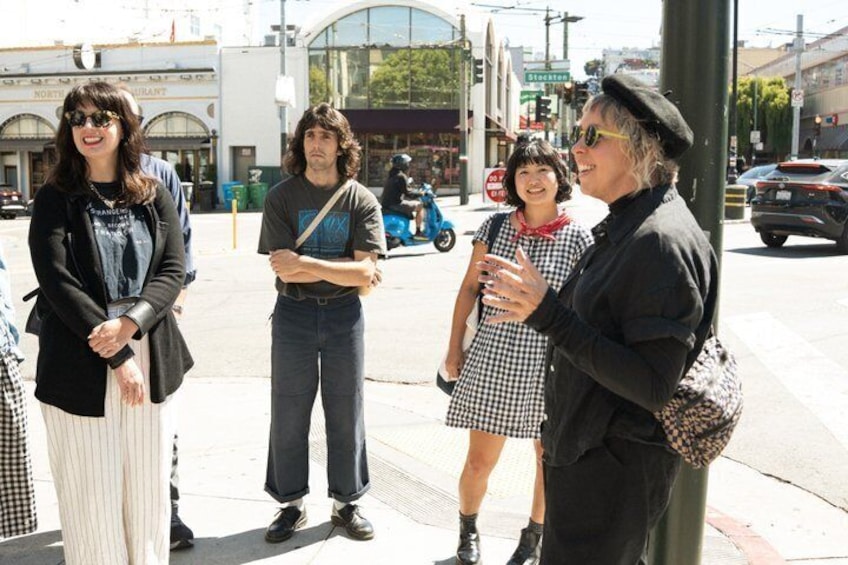 A group of people standing on a sidewalk, a street with cars, and a building with a sign that reads 'Northwest Restaurant'. 3