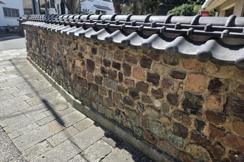A stone wall with a tiled roof, a paved sidewalk, and a residential building in the background. 5