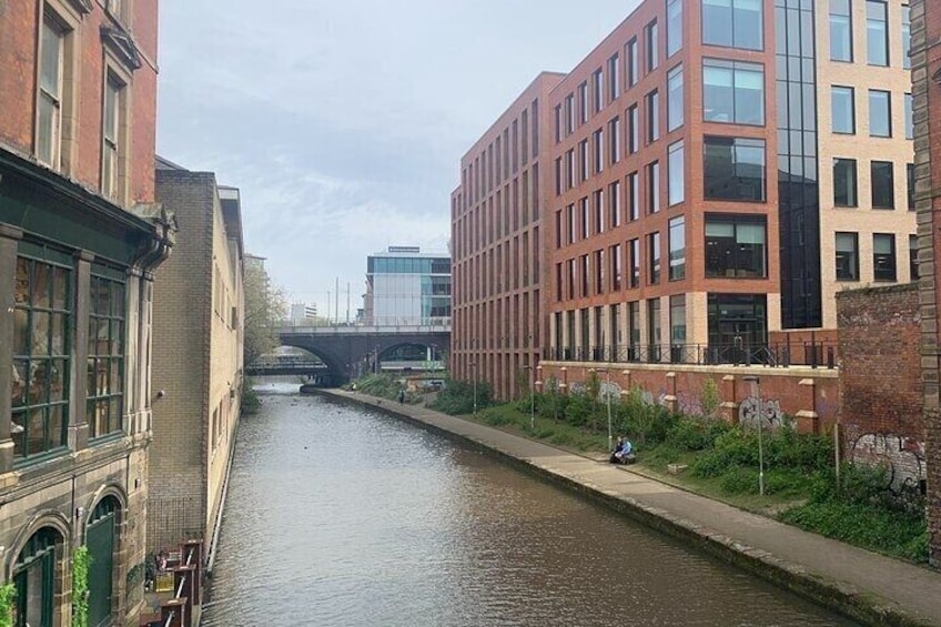 A canal flanked by buildings, a bridge in the distance, and a cyclist on the sidewalk. 3