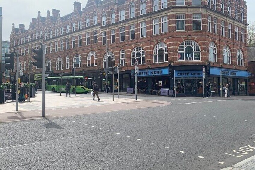 A street corner with a bus stop, a green bus, and a building with shops. 4