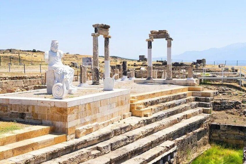 Ancient ruins with a seated statue, columns, and stone steps. 4