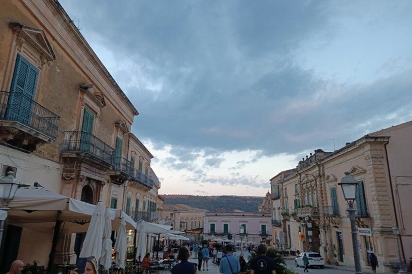 A bustling street with historic buildings, outdoor seating, and a crowd of people. 3
