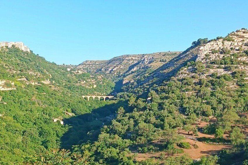 A valley with a bridge, green hills, and a clear sky. 5