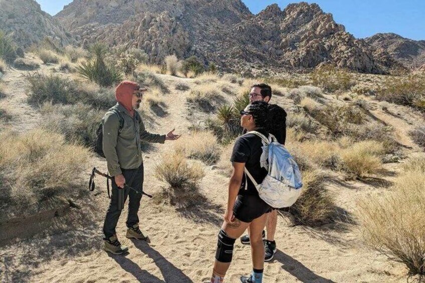 Three people hiking in a desert with mountains in the background. 3
