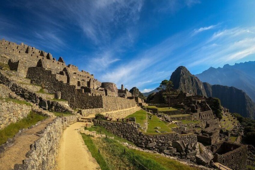 The ruins of Machu Picchu with stone walls, a dirt path, and mountains in the background. 3
