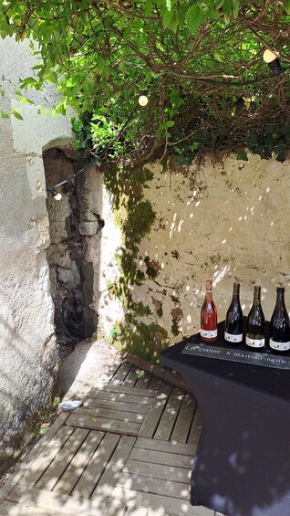 A rustic outdoor setting with a stone wall, wooden steps, and a table with wine bottles. 4