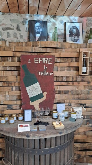 A rustic wooden bar with a large poster advertising 'EPIRE le meilleur' and various bottles and jars of wine. 2