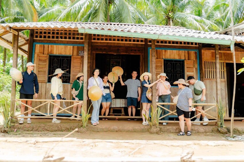 A group of people standing in front of a wooden building with a tiled roof, surrounded by palm trees. 3