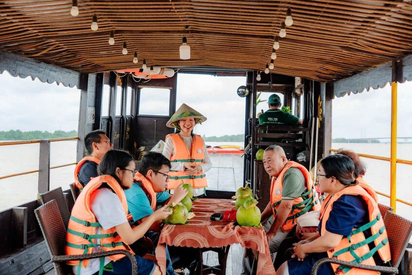 A group of people on a boat, wearing life jackets, gathered around a table with coconuts and a tablecloth. 1