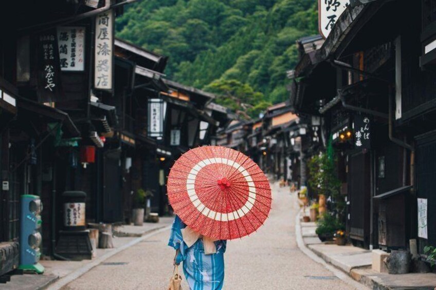 A traditional Japanese street with wooden buildings and a person holding a red umbrella. 3