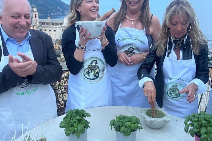 Four people wearing aprons with a logo, standing around a table with basil plants and a bowl. 4