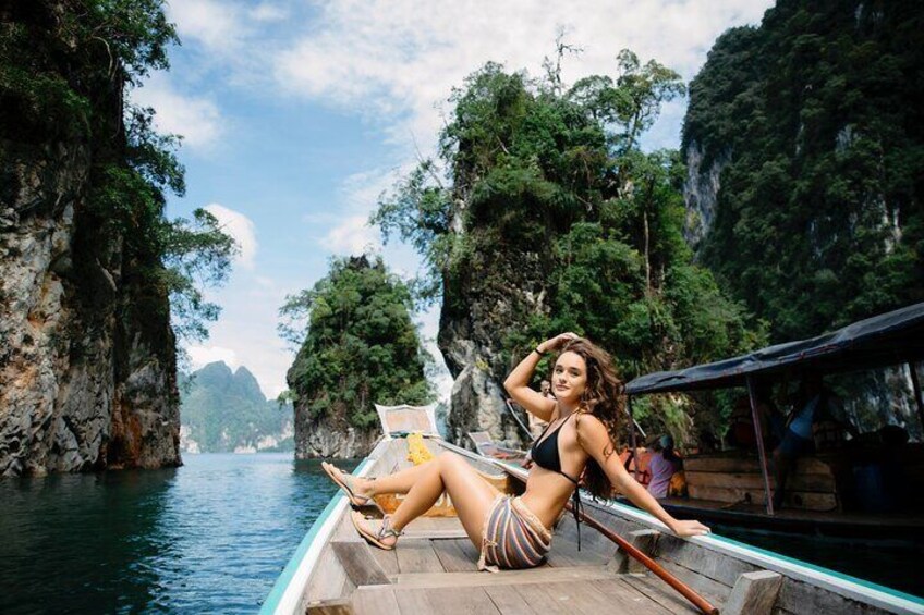 A person sitting on a boat in a tropical setting with rocky cliffs and greenery in the background. 5