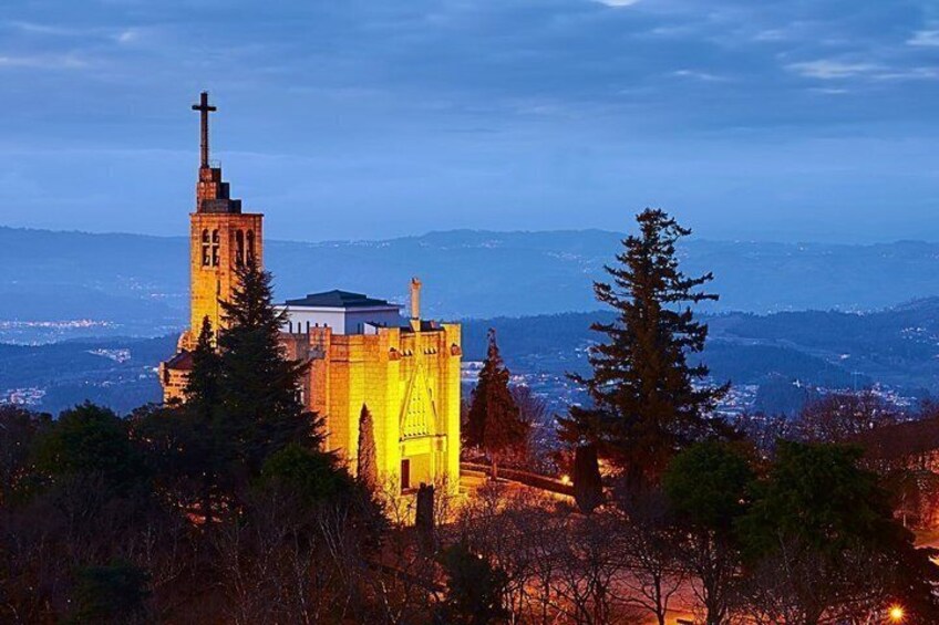 A church with a tall bell tower and a cross, surrounded by trees and mountains in the background. 2