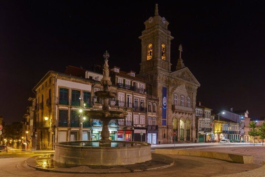 A historic building with a clock tower, a fountain, and illuminated storefronts. 4