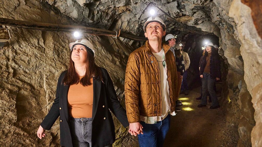 People in a tunnel with rocky walls and a wooden beam overhead. 5
