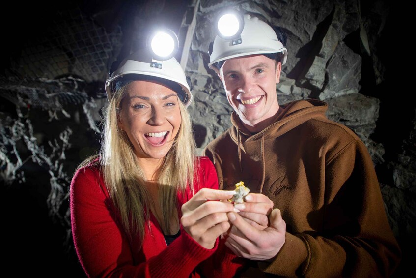 Two people in a cave wearing helmets with lights, holding a piece of rock. 4
