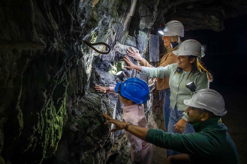 A group of people wearing hard hats and safety gear, inspecting a rocky cave wall. 3