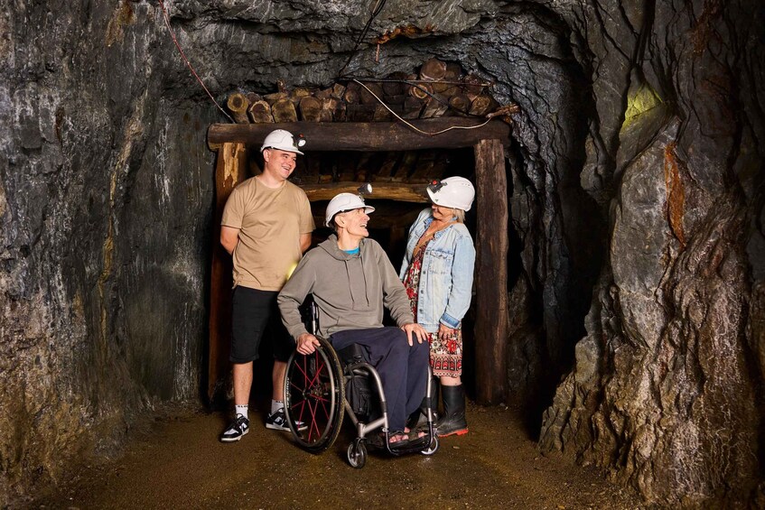 Three people in a cave with rocky walls and a wooden structure overhead. 2
