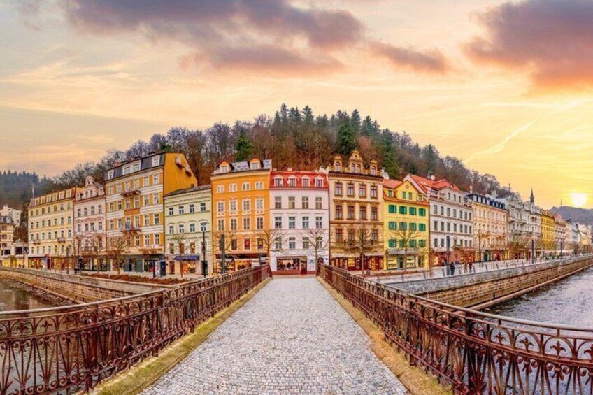A river with a cobblestone path, colorful buildings, and a metal bridge railing. 3