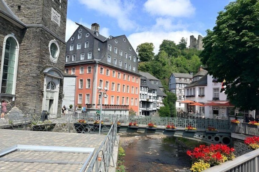 A riverside walkway with historic buildings, a stone bridge, and a castle in the background. 2