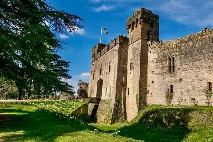 A historic stone castle with a flag, surrounded by greenery and a clear sky. 2