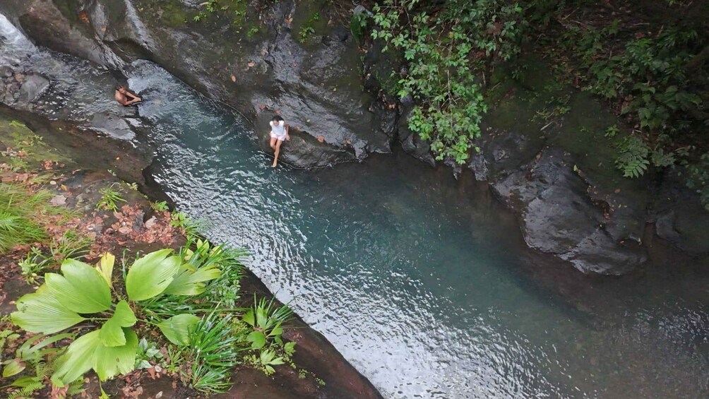 A narrow water channel with rocky banks, surrounded by lush greenery. 1