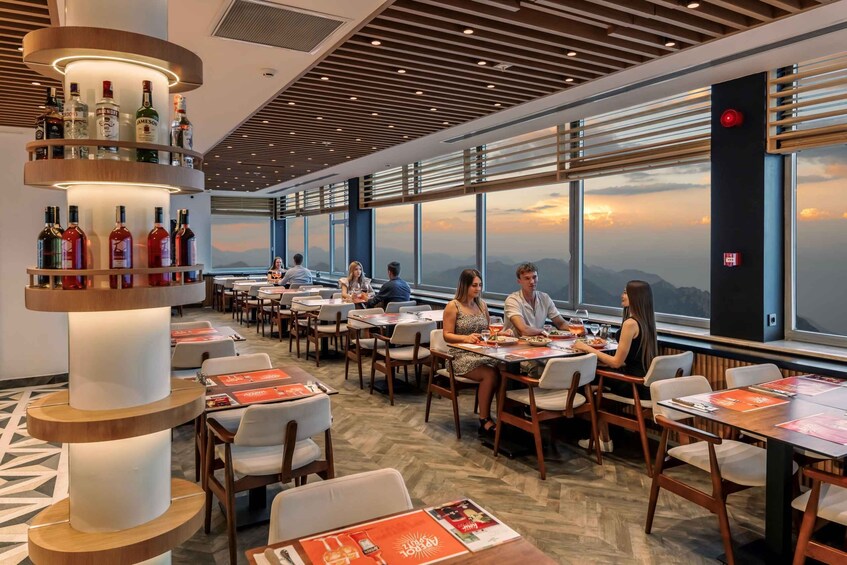 A restaurant with tables and chairs, a bar with bottles, and a view of the mountains through large windows. 2