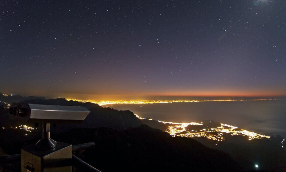 A telescope overlooking a city at night with a starry sky. 5