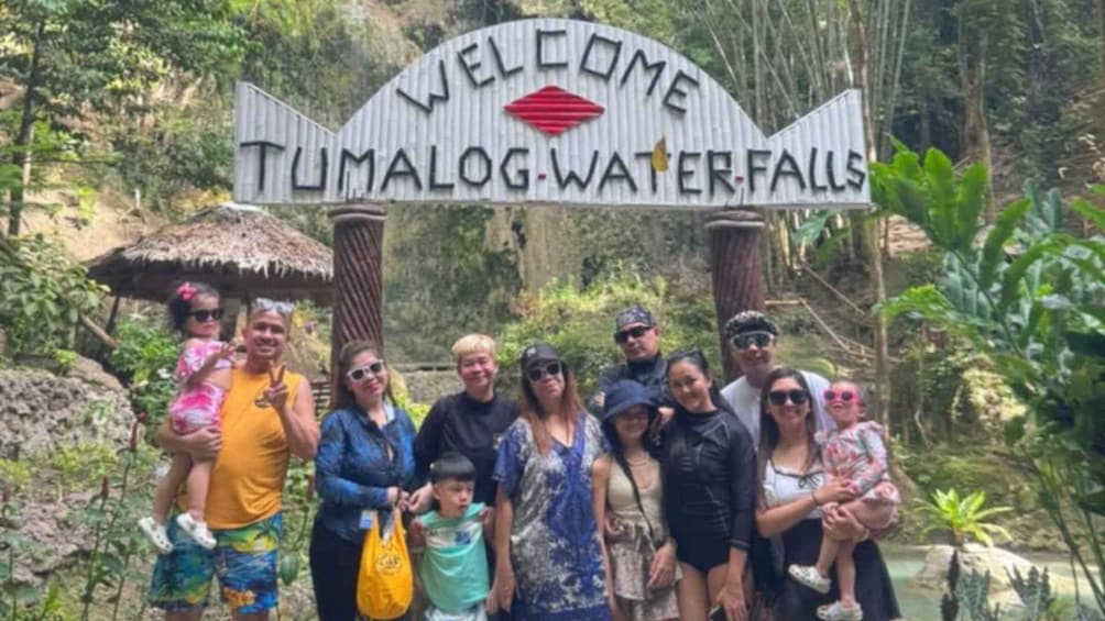 A group of people posing in front of a sign that reads 'Welcome to Tumalog Waterfalls.' 3